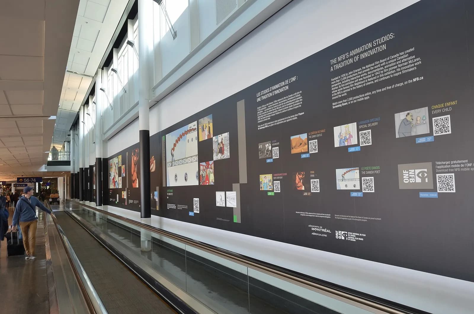 un trottoir roulant longé d'un mur d'exposition dans un couloir de l'aéroport de Montréal