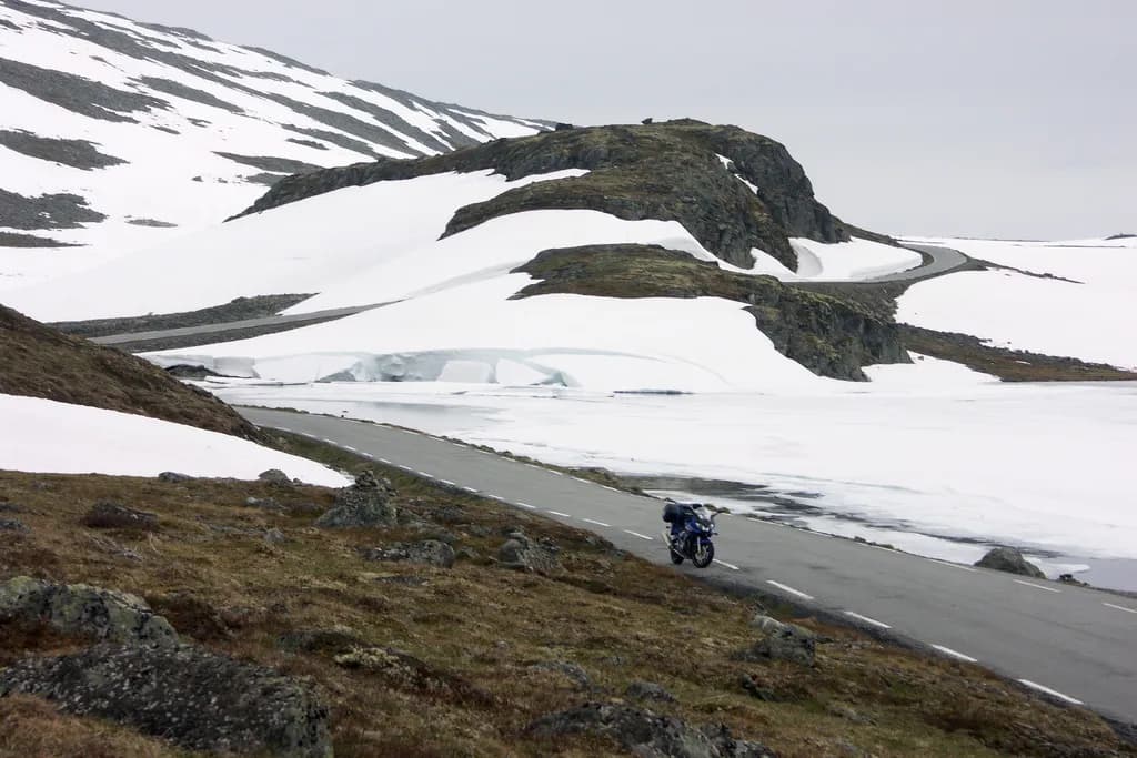 motard sur la route d'Aurlandsfjellet serpentant entre roches et plaques de neige