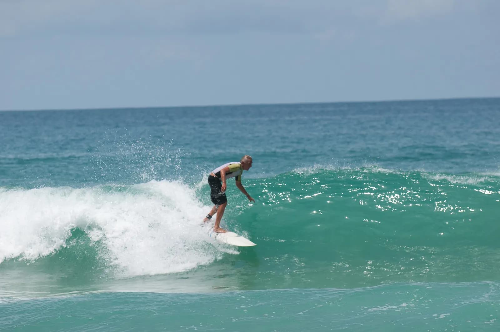 un surfeur sur une vague turquoise à Surin Beach, la plage voisine de Kamala à Phuket