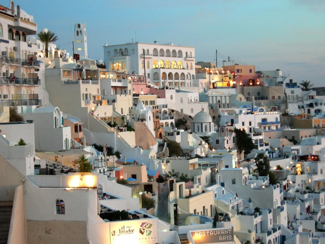 the houses of Fira lighting up one by one as night falls over the caldera