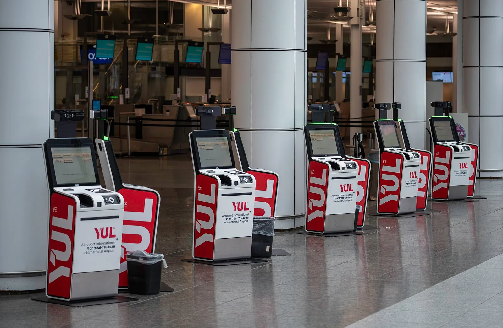 bornes d'enregistrement libre-service rouges et blanches alignées dans l'aéroport de Montréal