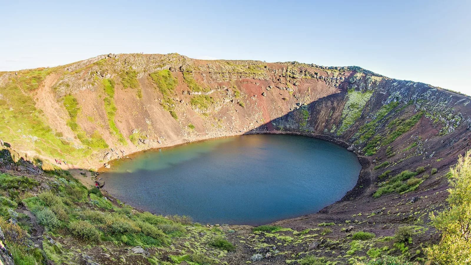panorama du cratère de Kerið avec son lac bleu profond et ses pentes de scories rouges
