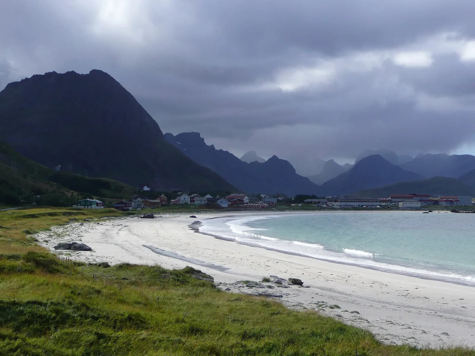 la plage de sable blanc de Ramberg en croissant, avec le village et les montagnes en arrière-plan