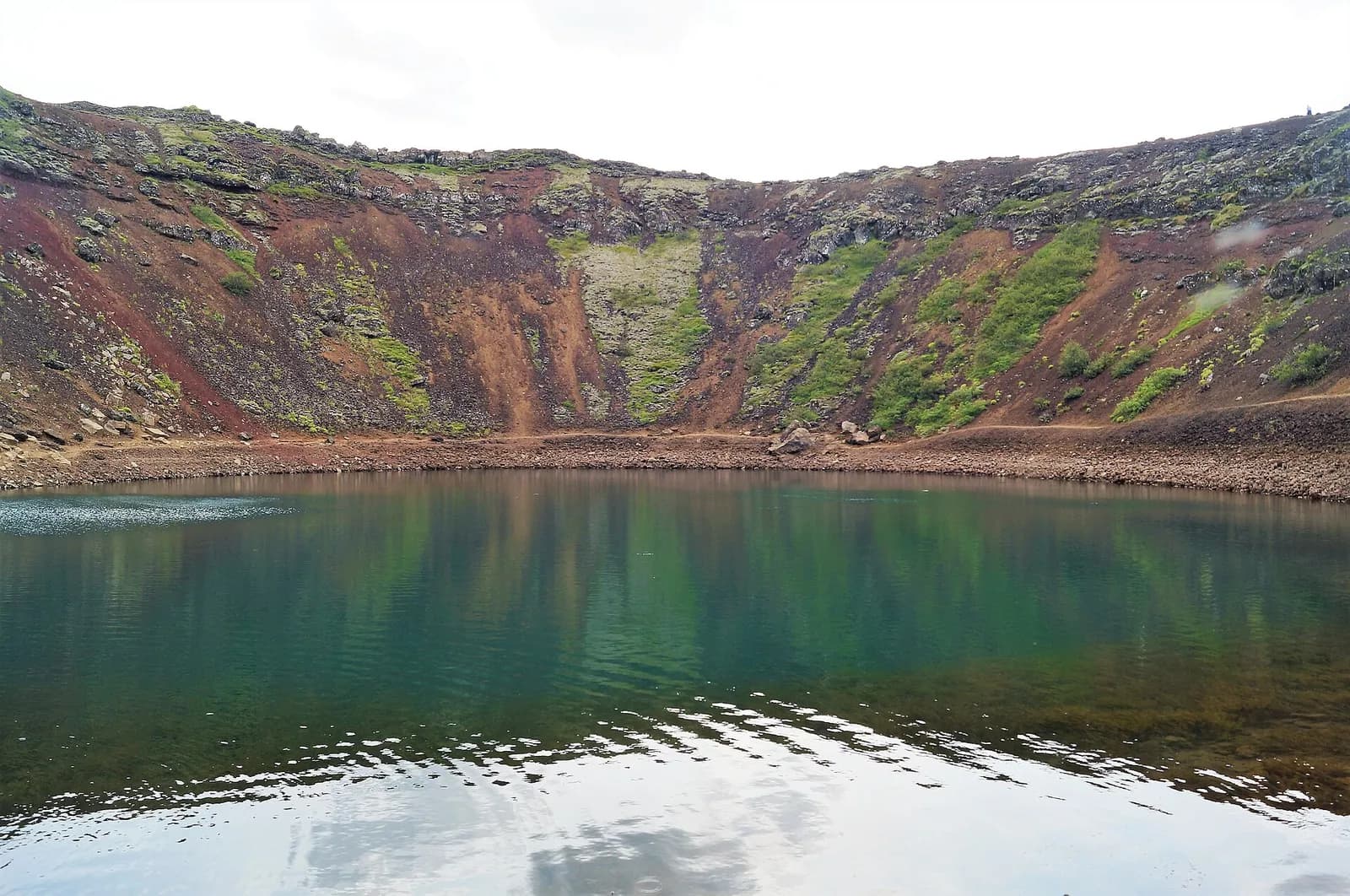au bord de l'eau au fond du cratère de Kerið, face aux parois de roche volcanique