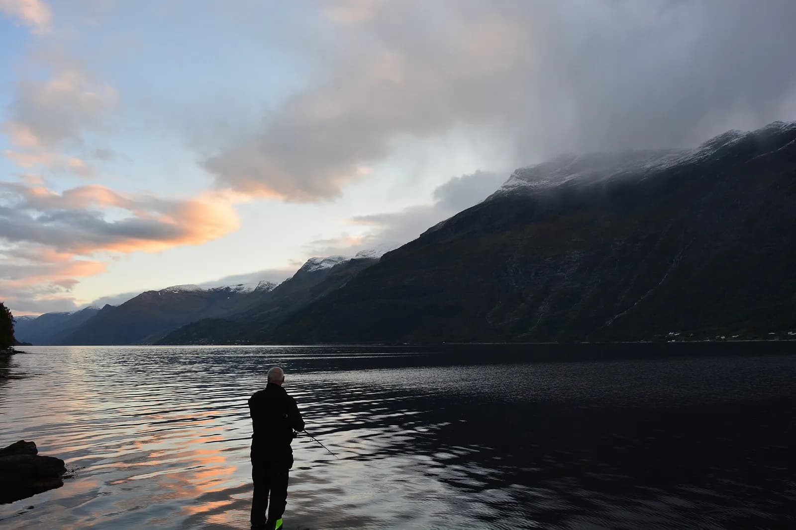pêcheur au bord d'un fjord norvégien sous un ciel nuageux au crépuscule