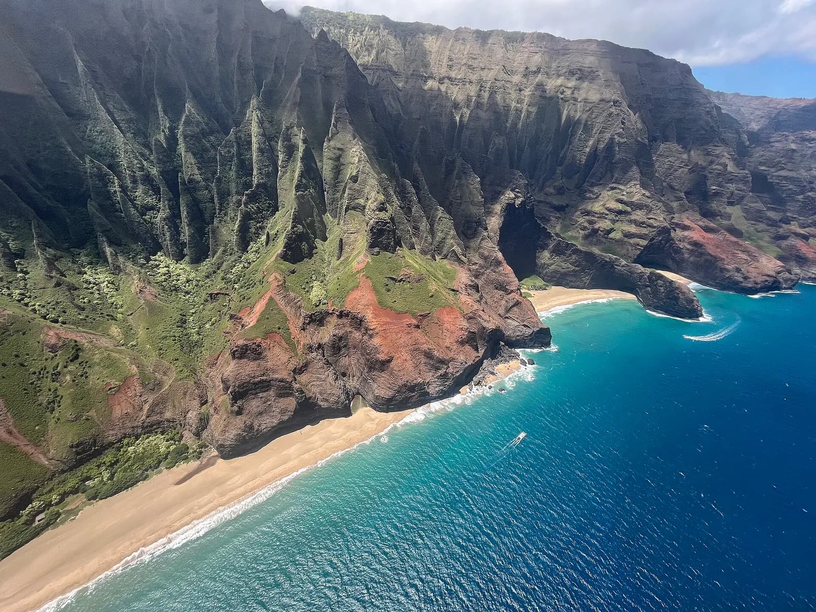 les falaises vertes de la côte de Nā Pali plongent vers une plage de sable à Kauai