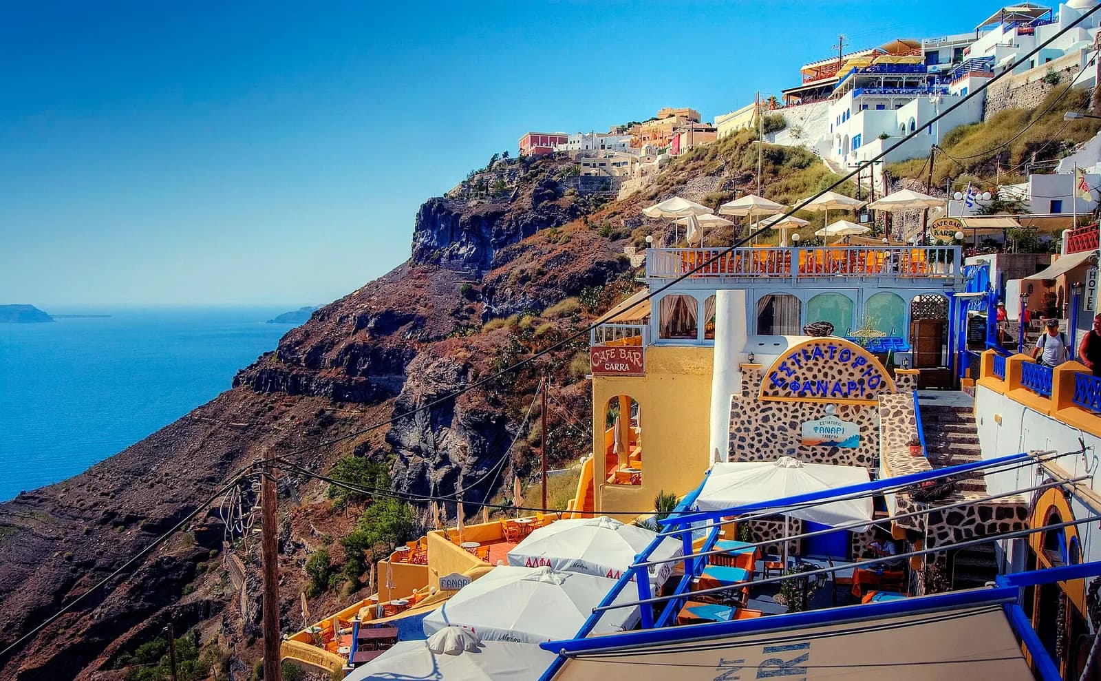 a taverna with white parasols clinging to the Santorini cliffside