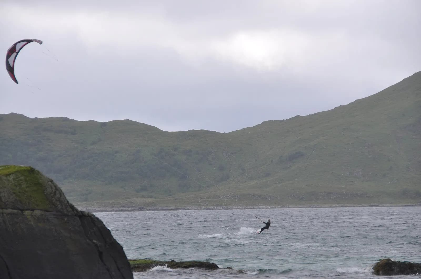 kitesurfeur glissant sur l'eau dans la baie de Haukland, entourée de collines verdoyantes