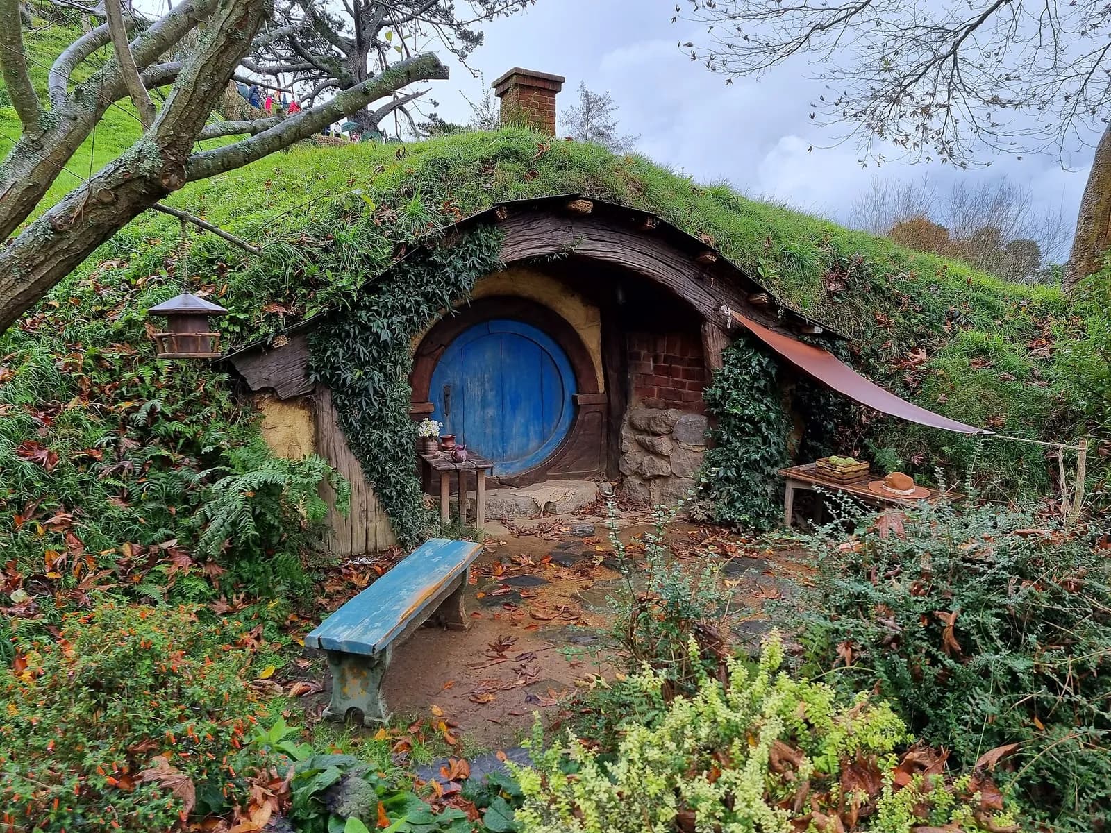 un trou de hobbit à la porte bleue et son banc en bois sous la verdure de la Comté