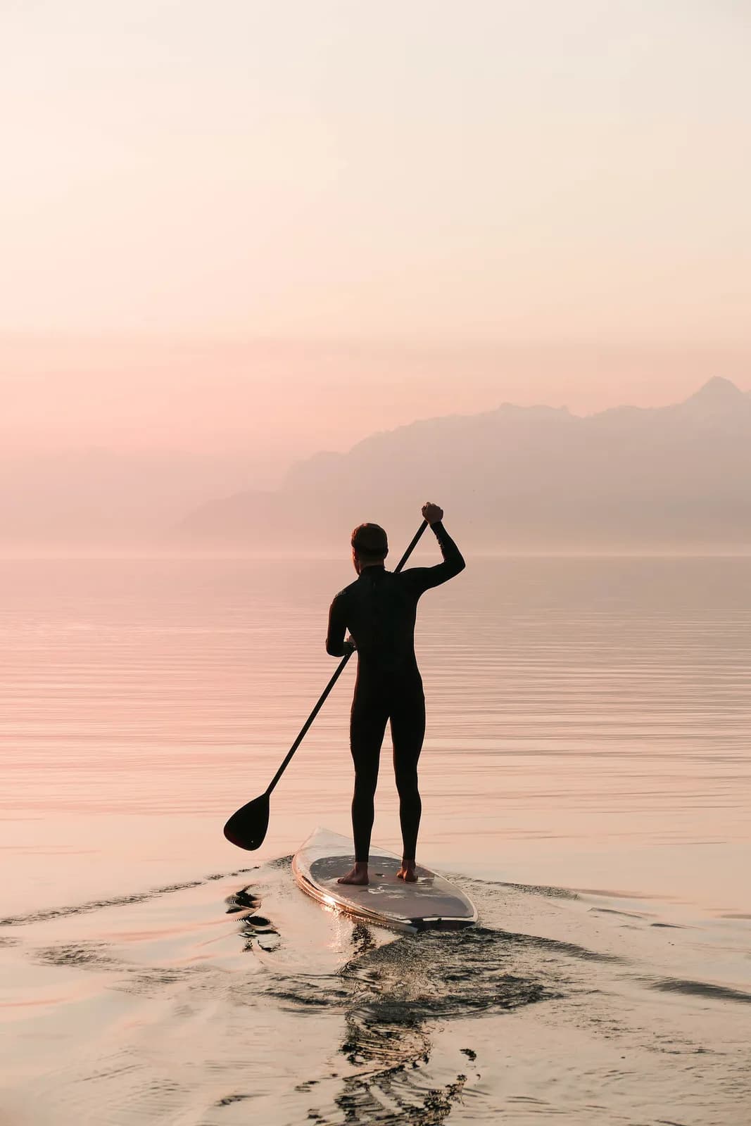 silhouette d'un paddleur debout sur un lac alpin aux eaux calmes dans la brume