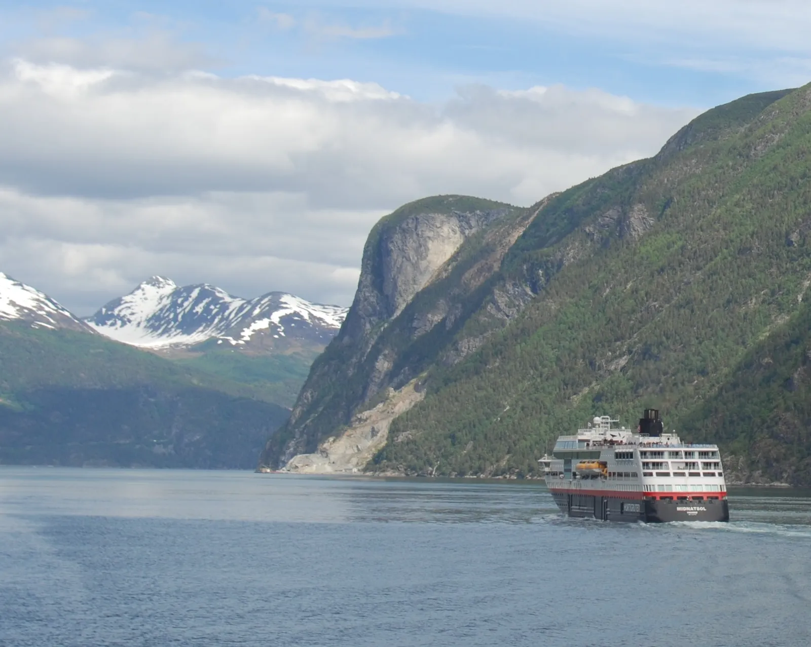 navire de croisière naviguant dans un fjord encadré de montagnes escarpées
