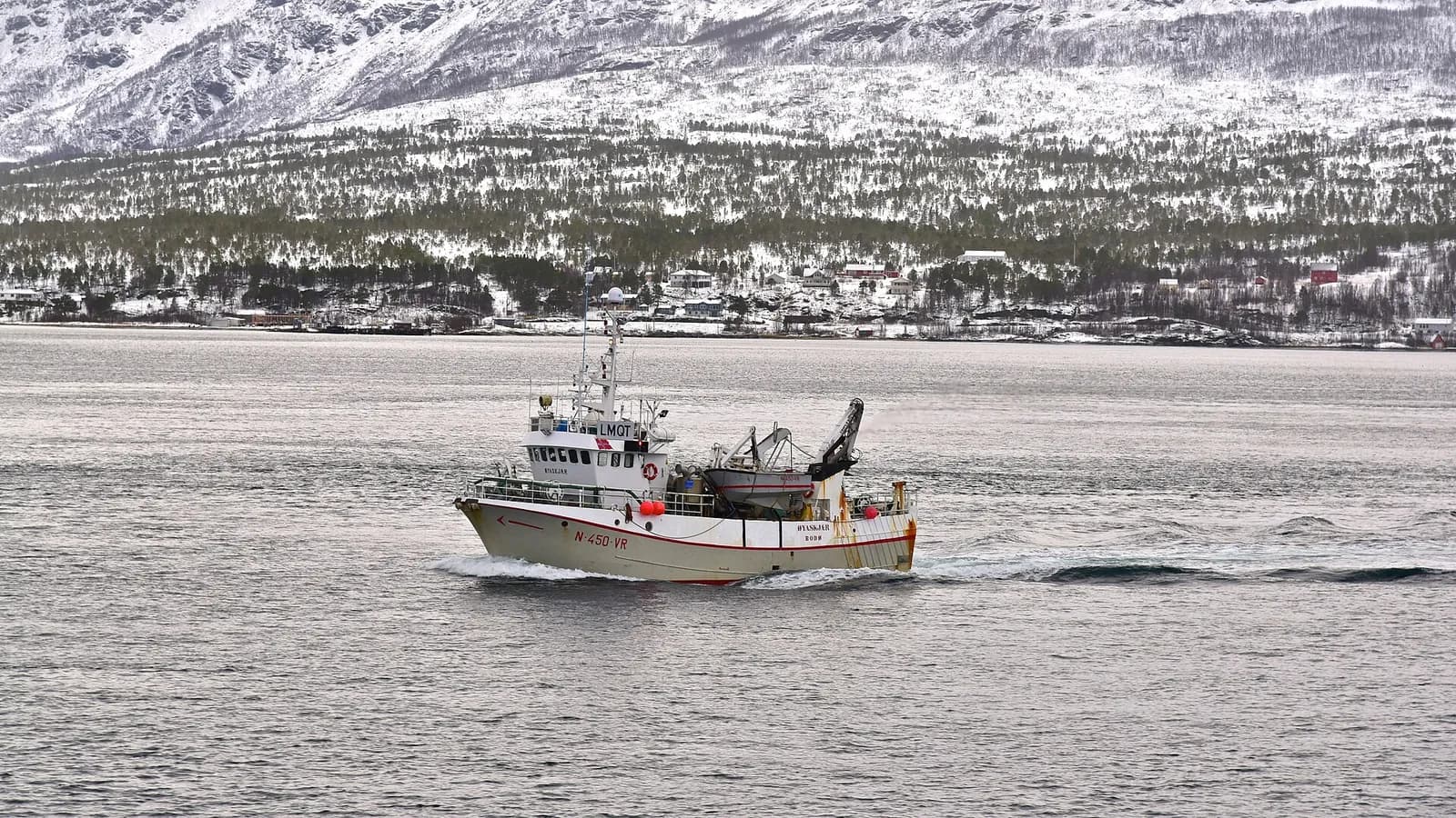 bateau de pêche naviguant dans le détroit de Tromsø devant la côte enneigée