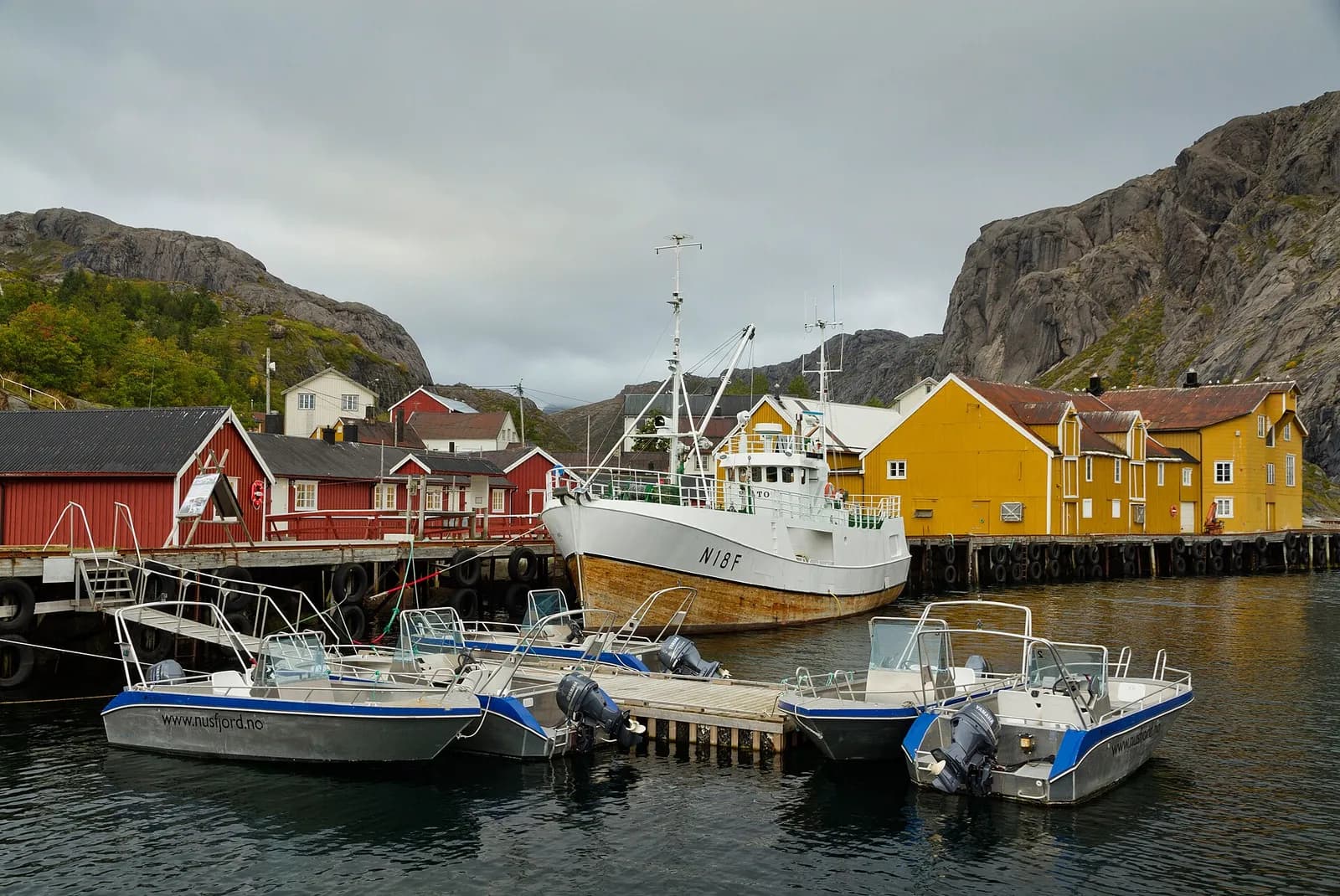 bateaux de pêche amarrés devant les maisons jaunes et rouges du port de Nusfjord