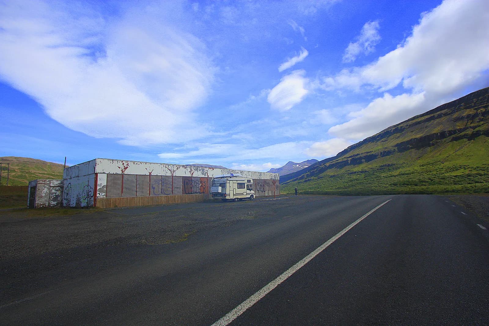 camping-car stationné au bord d'une route déserte, face à un fjord et des montagnes verdoyantes
