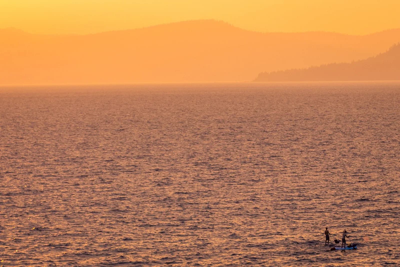 paddleurs sur un lac baigné par la lumière orangée du coucher de soleil