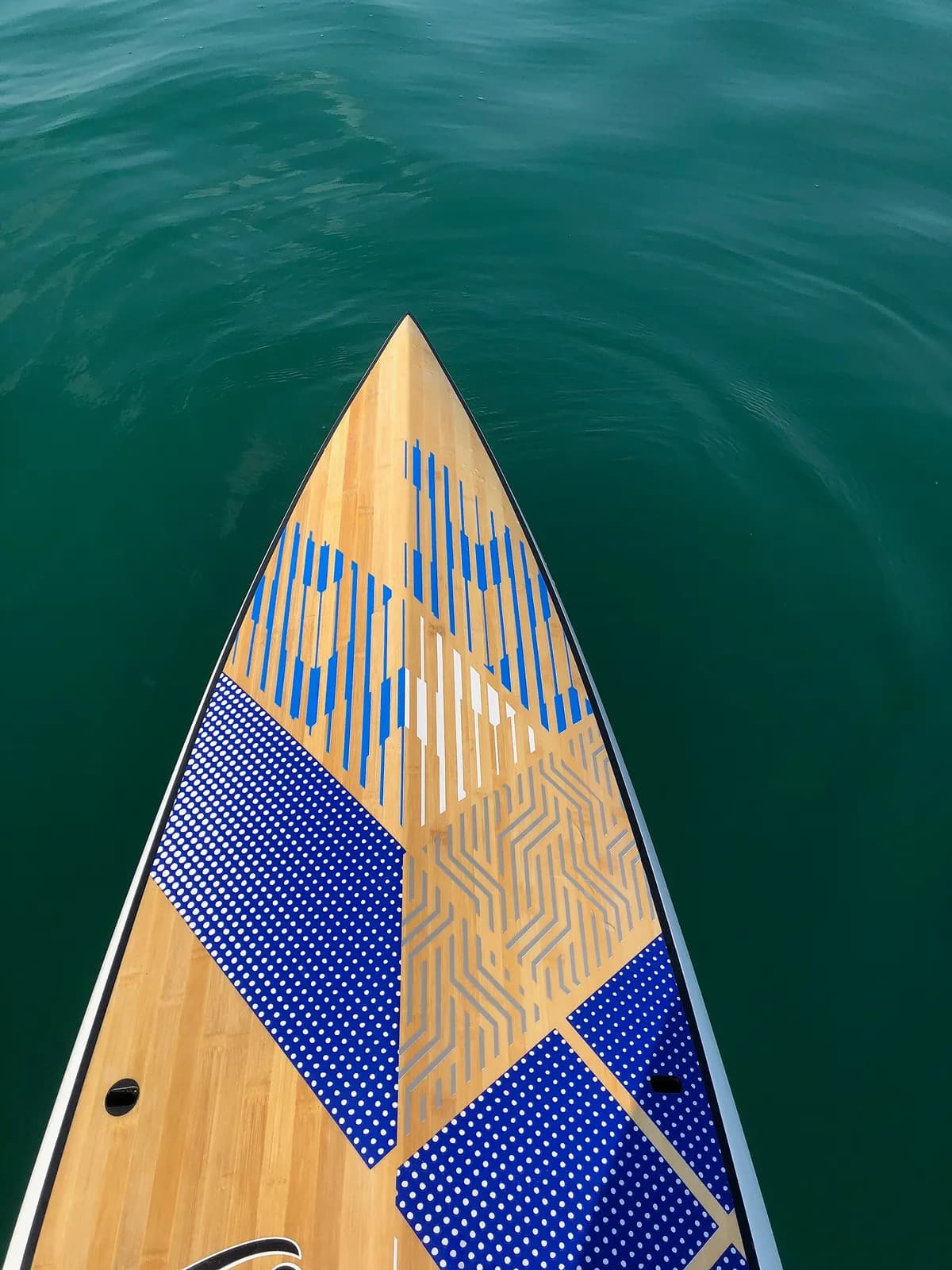 avant d'une planche de paddle en bois glissant sur une eau vert émeraude