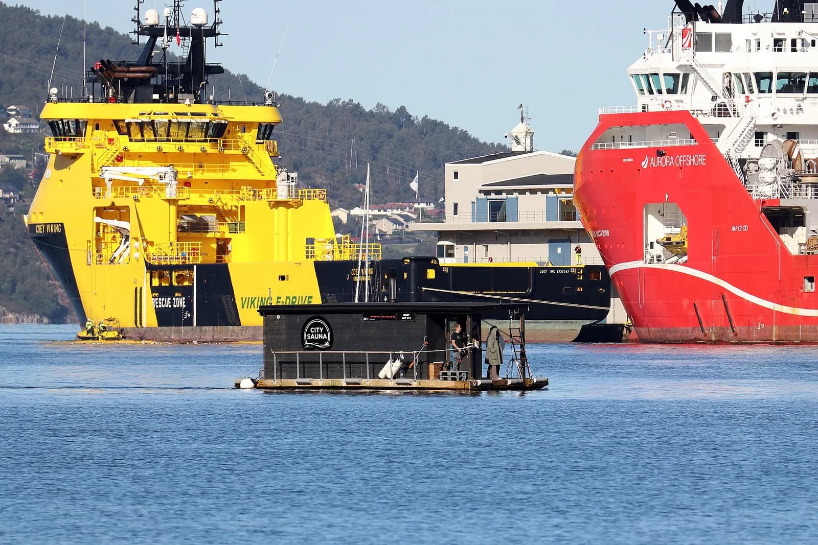 sauna flottant sur le port de Bergen, avec des navires de ravitaillement en arrière-plan