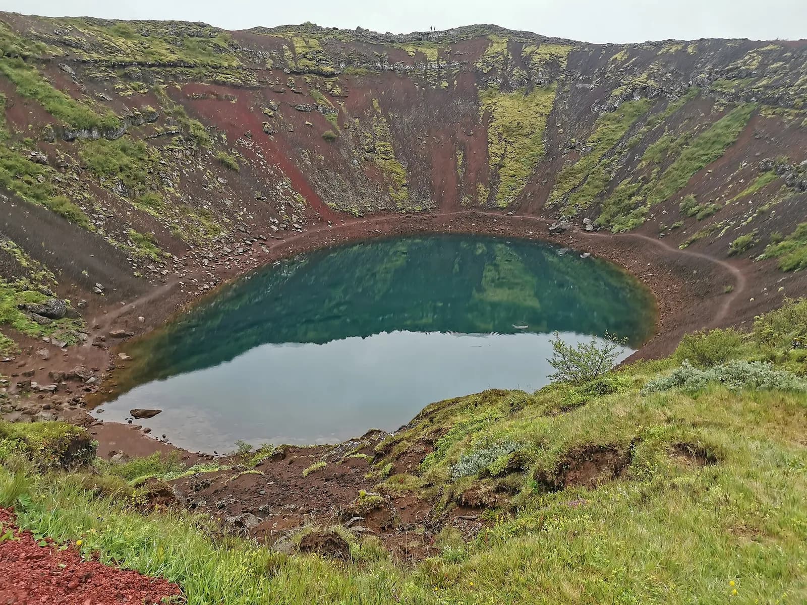 le lac de Kerið reflétant le ciel au fond du cratère aux pentes rouges et vertes