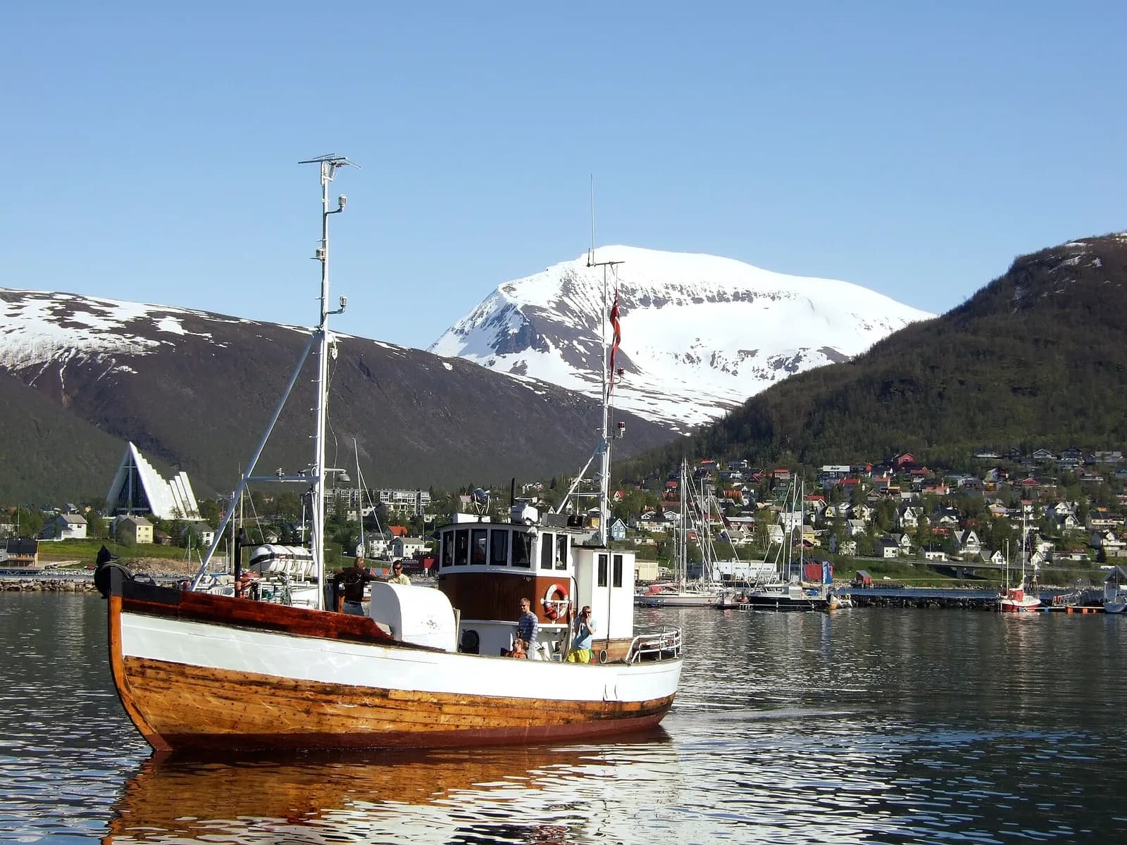 bateau de pêche en bois dans le port de Tromsø en été, face aux montagnes et à la cathédrale arctique