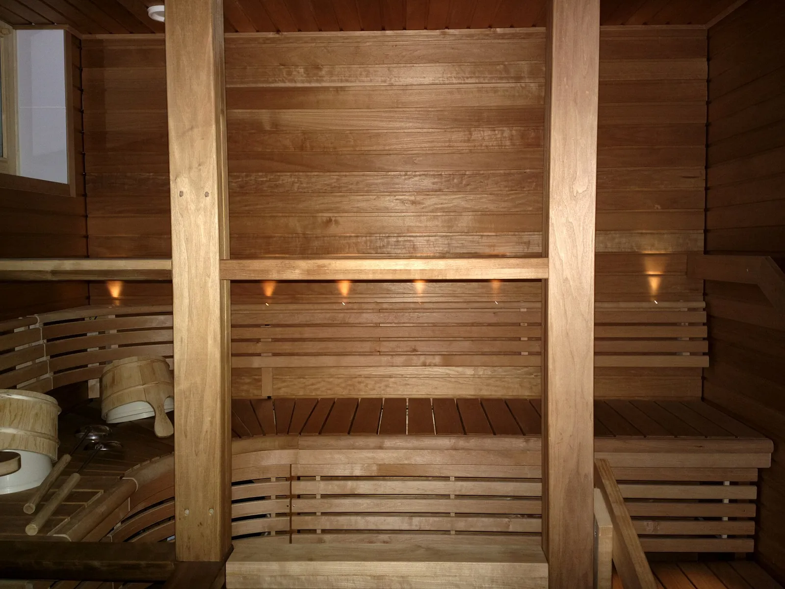 intérieur d'un sauna en bois clair avec ses bancs en gradins et un seau en bois