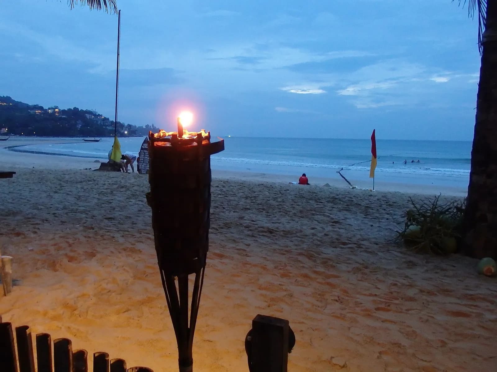 une torche allumée sur le sable de Kamala Beach à la tombée de la nuit