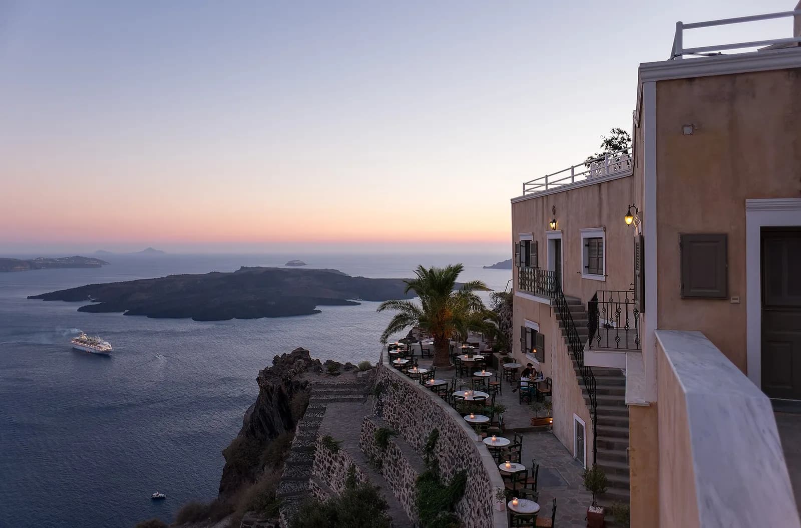 a clifftop restaurant terrace in Fira at sunset, overlooking the caldera