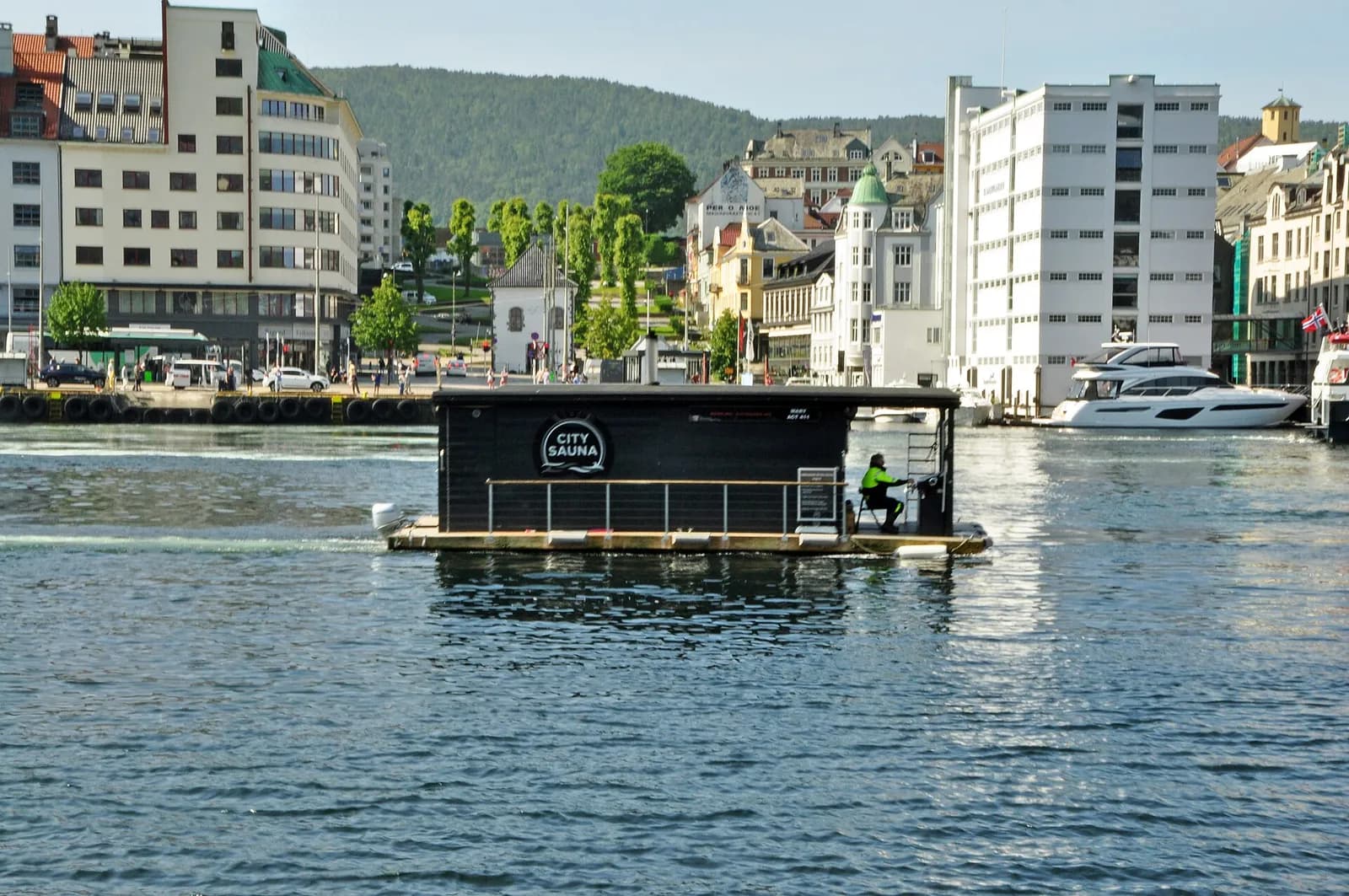 sauna flottant en bois sombre sur les eaux du port de Bergen, devant les immeubles du quai