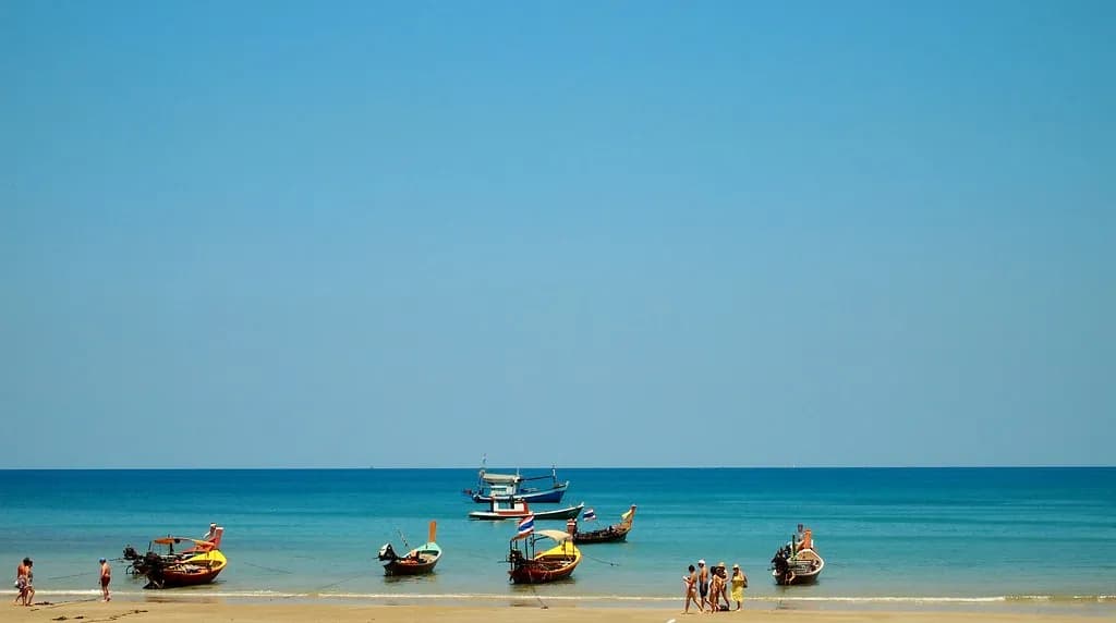 bateaux longtail colorés sur l'eau turquoise de Kamala Beach sous un grand ciel bleu