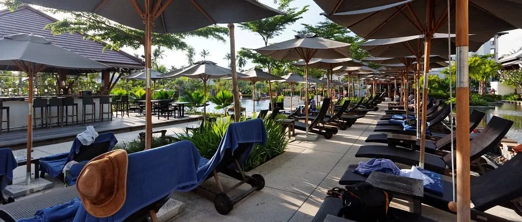 transats et parasols au bord de la piscine d'un resort tropical en Thaïlande