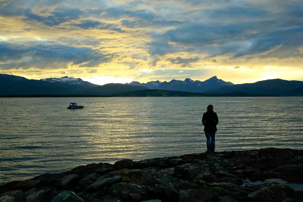 silhouette sur un rivage rocheux de Tromsø face au fjord et aux montagnes dans la lumière du soir