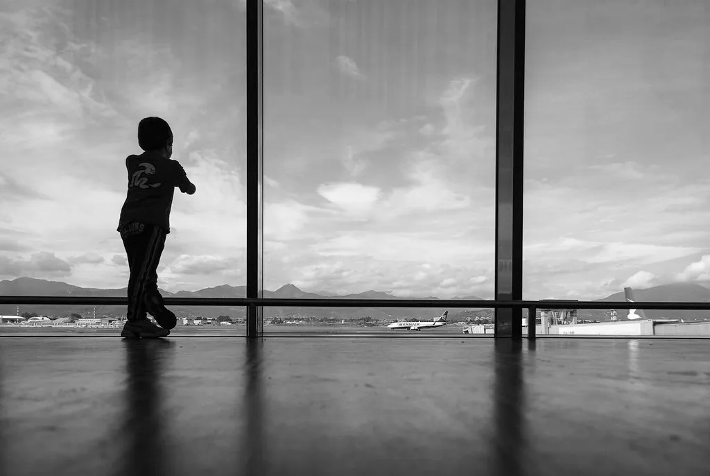 silhouette d'un enfant regardant les avions à travers la grande baie vitrée d'un aéroport