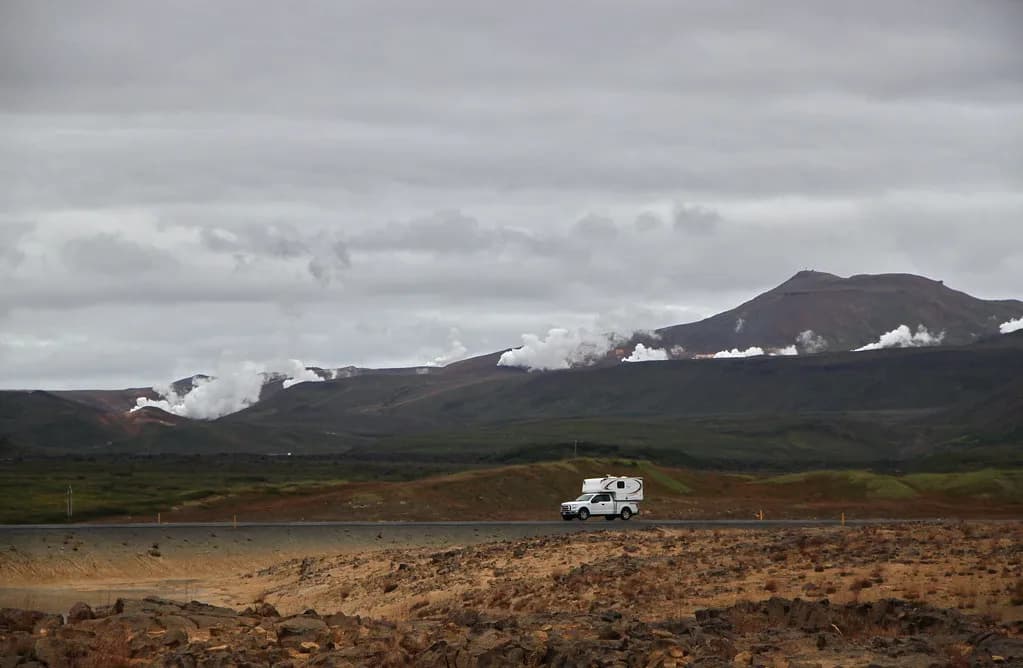 camping-car roulant sur une piste islandaise au pied de montagnes fumantes de fumerolles