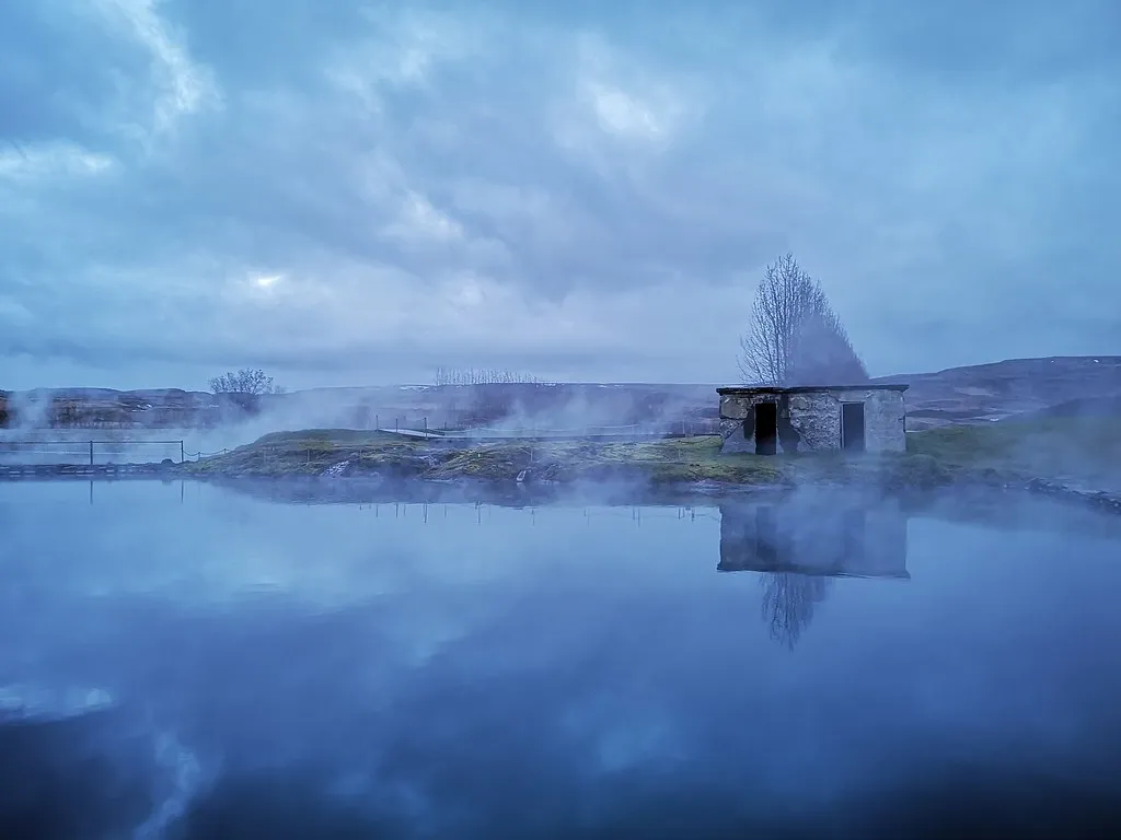 le Secret Lagoon de Flúðir fumant à l'aube, avec sa cabane en pierre au bord de l'eau
