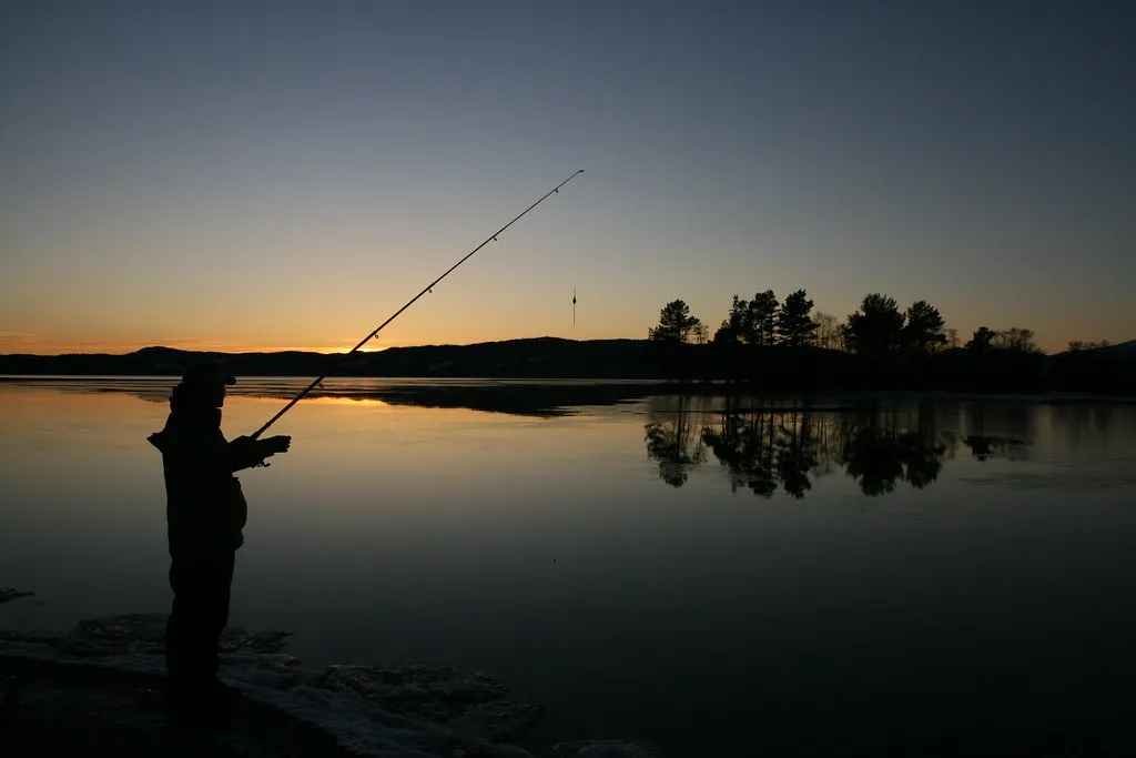 pêcheur lançant sa ligne dans un lac norvégien au coucher du soleil