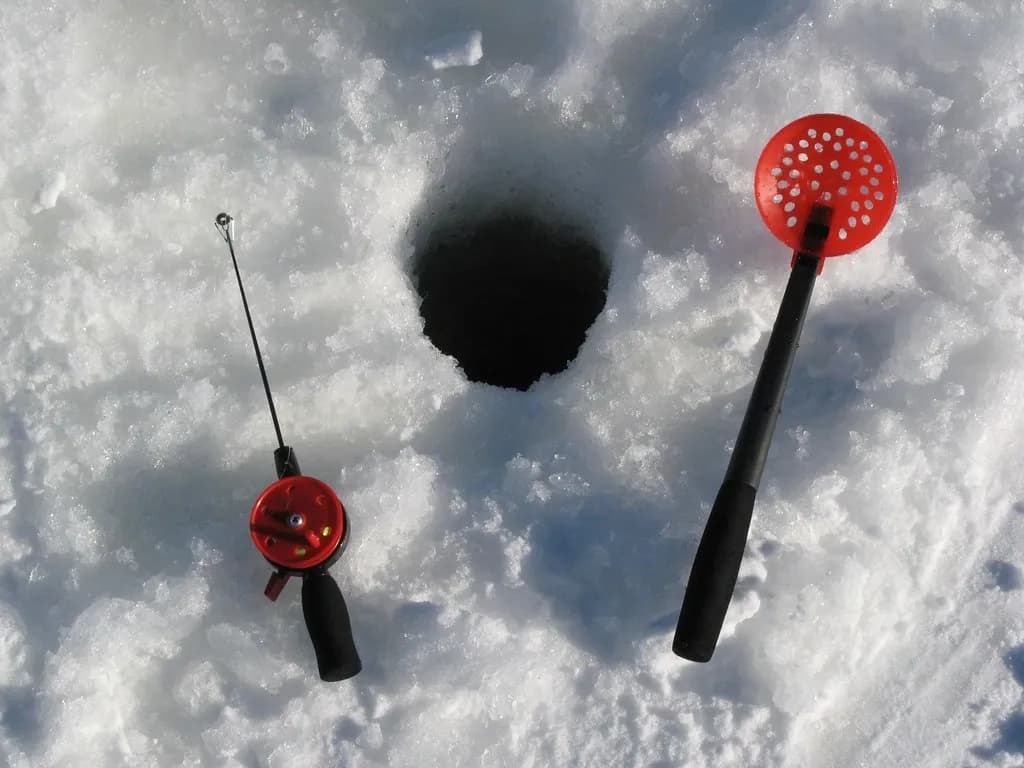 canne de pêche blanche et écumoire posées près d'un trou dans la glace