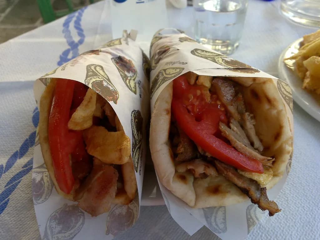 two gyros pitas filled with meat, tomatoes and fries, wrapped in paper