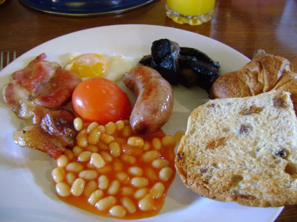 a full breakfast plate with bacon, sausage, beans and bread