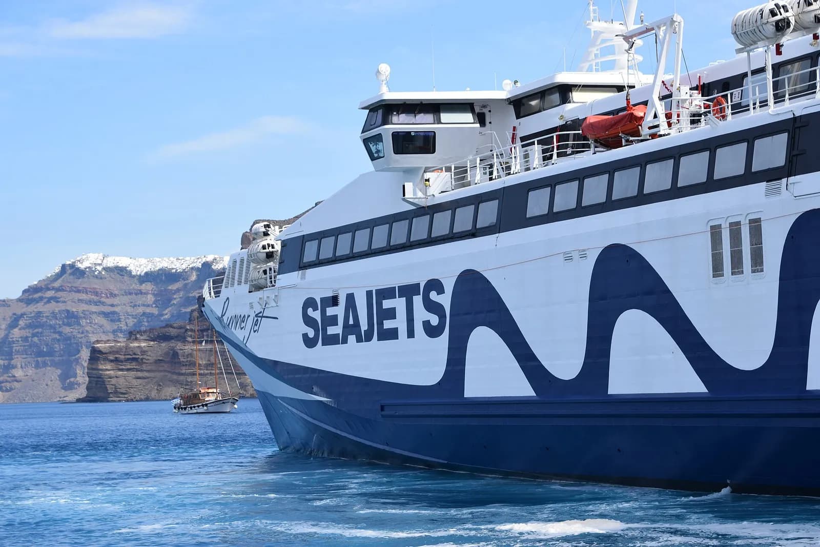 Un catamaran SeaJets accoste à Athinios, avec les falaises blanches de la caldeira de Santorin derrière