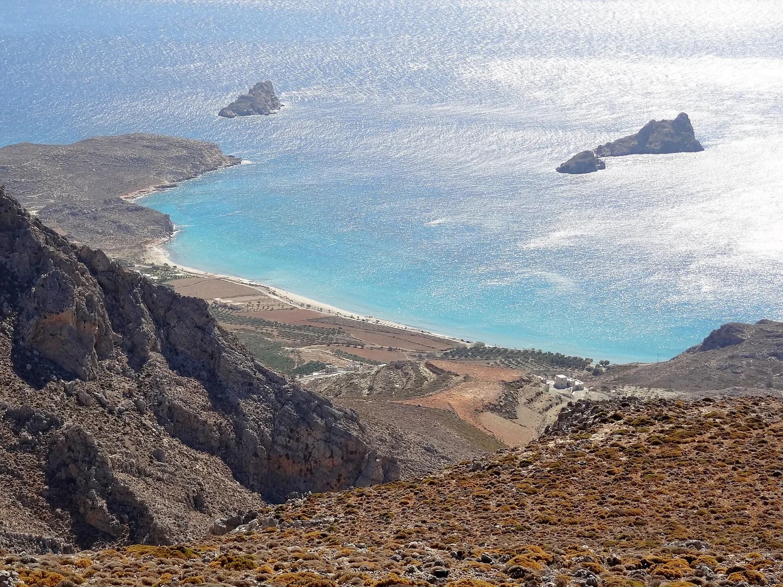 La baie turquoise de Xerokambos et sa plaine cultivée vues depuis les hauteurs, avec ses îlots au large