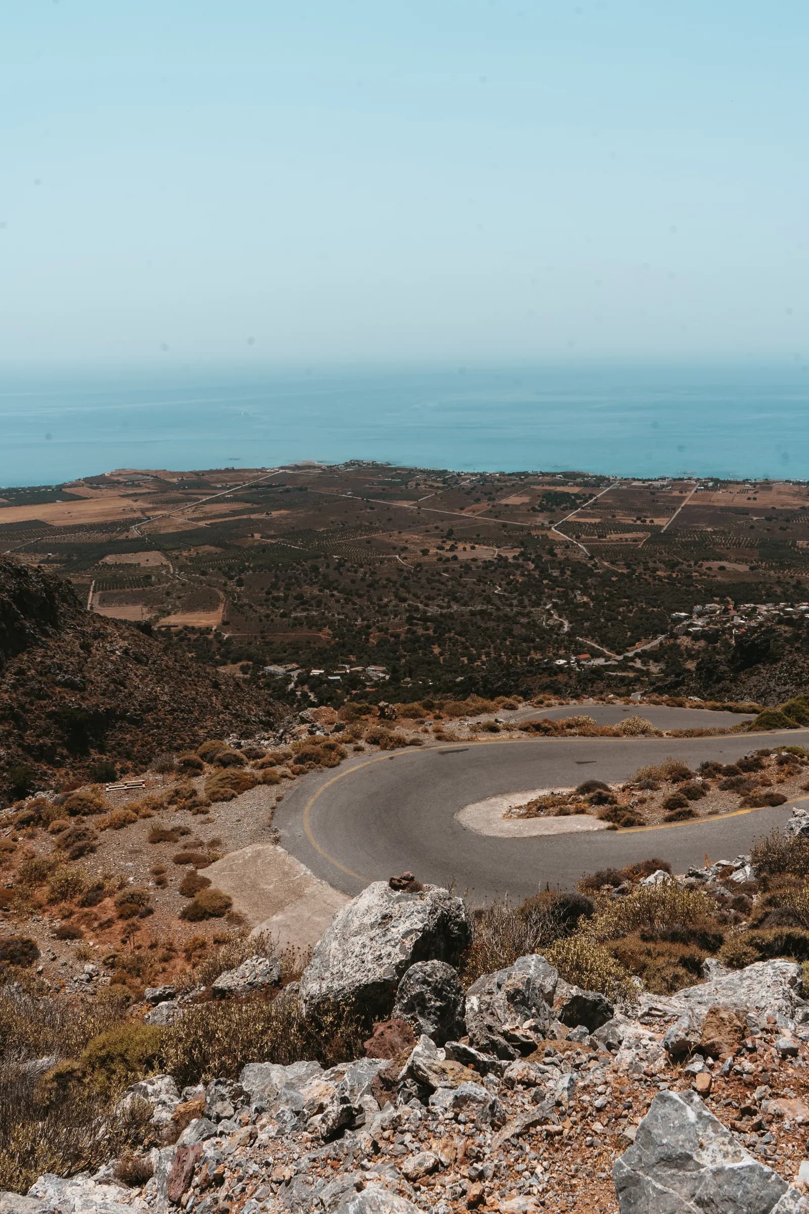 Route en lacets dans les collines sèches de la Crète, avec la mer bleue à l'horizon