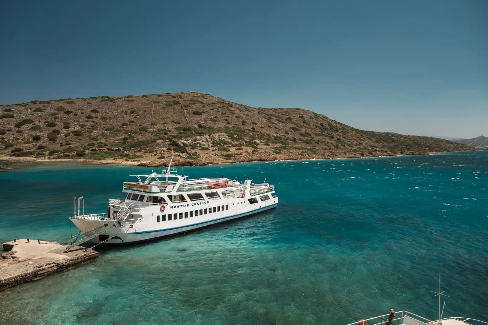 Bateau de croisière amarré à l'embarcadère de Spinalonga dans une eau turquoise