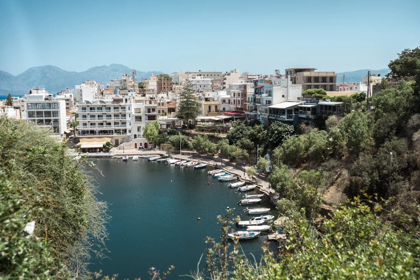 Le lac Voulismeni bordé de barques au pied des maisons d'Agios Nikolaos, montagnes à l'horizon