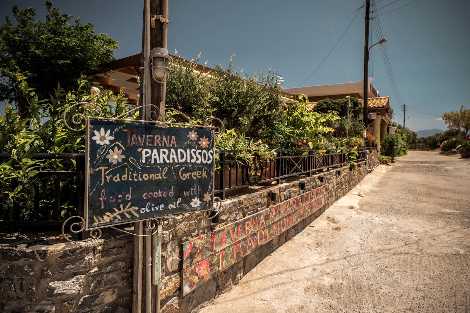 Ardoise peinte d'une taverne traditionnelle au bord d'une ruelle de village fleurie, dans la région d'Elounda