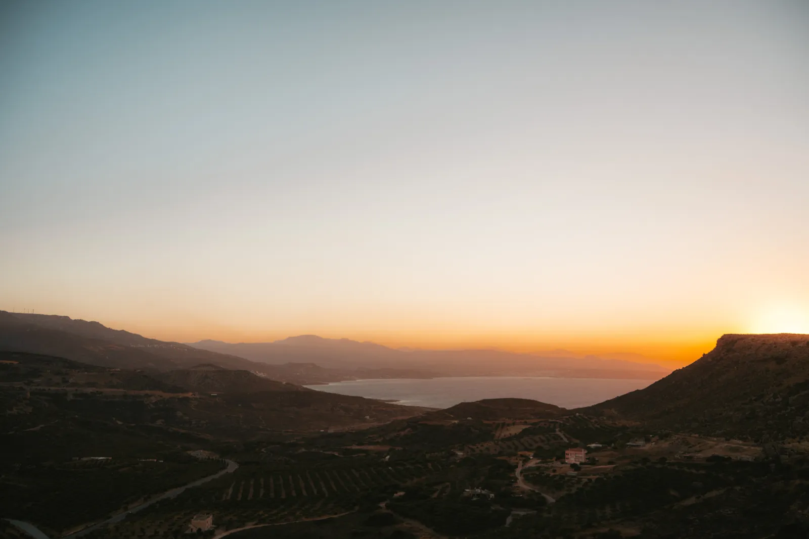 Collines plantées d'oliviers et baie au coucher du soleil, vues depuis une route de l'est de la Crète
