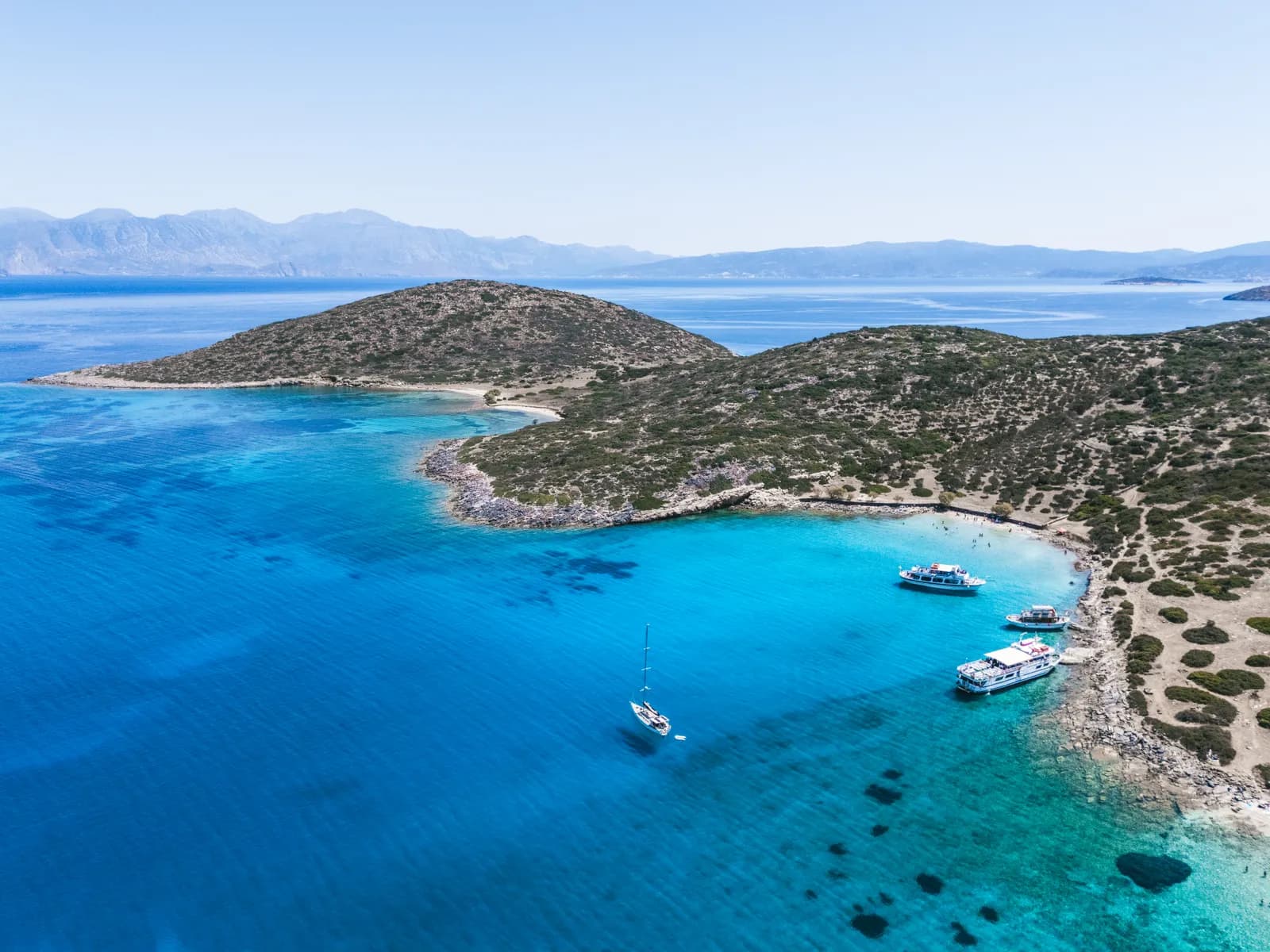Yachts mouillés dans une baie turquoise de la presqu'île de Spinalonga, face au golfe d'Elounda