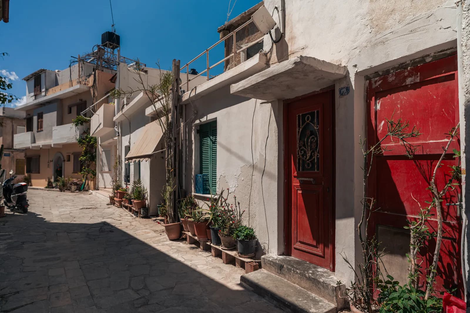 Narrow lane in Ierapetra old town with red doors and potted plants