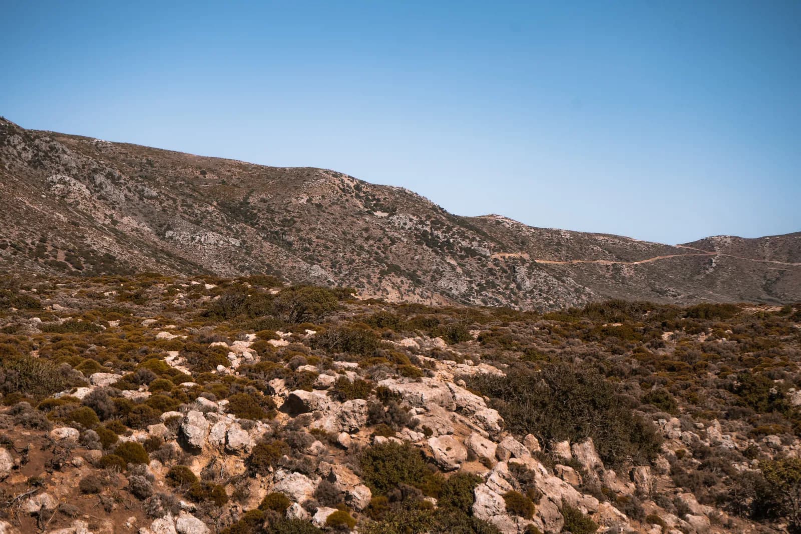 Dirt track winding along a mountainside through the scrubland of western Crete