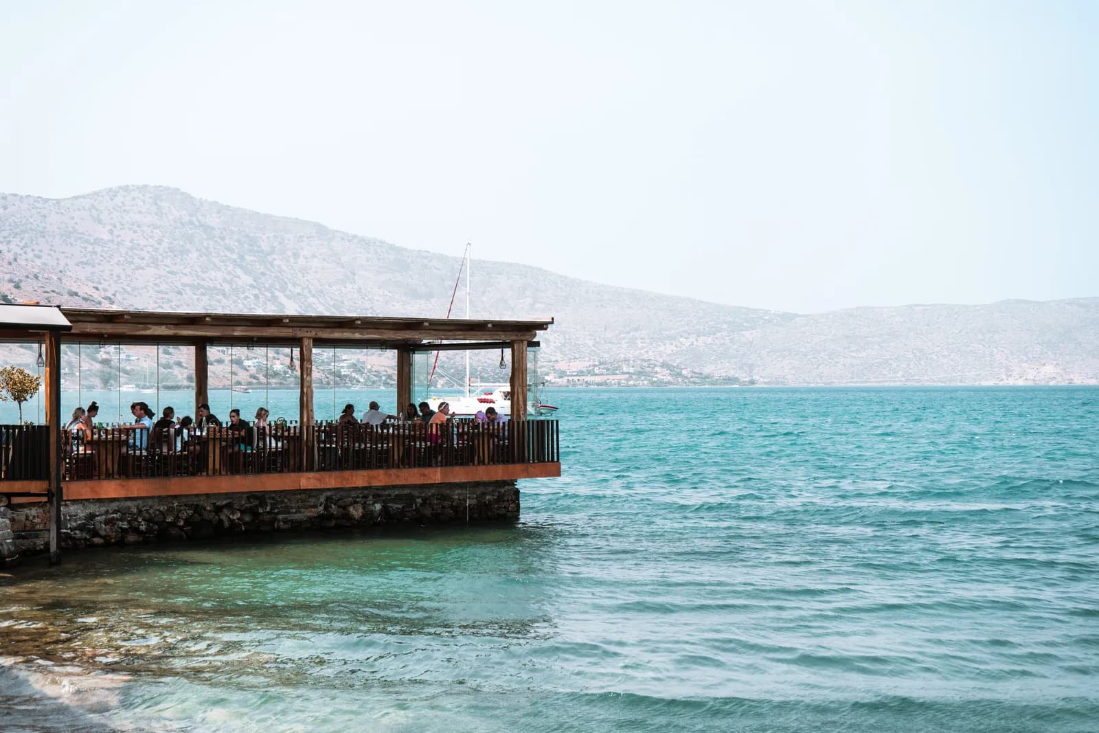 Taverna on stilts over the turquoise water of Elounda bay, facing the hills