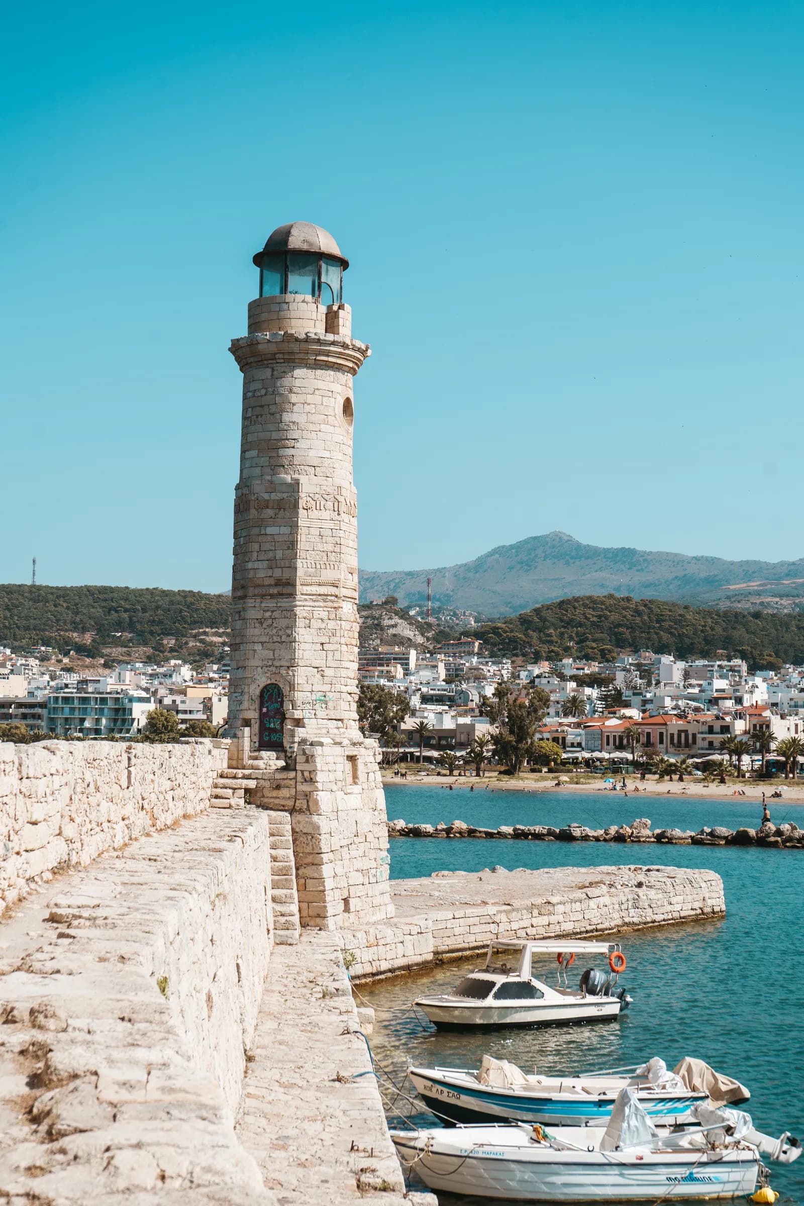 Le phare vénitien du port de Réthymnon sur sa jetée de pierre, avec la ville et les collines derrière