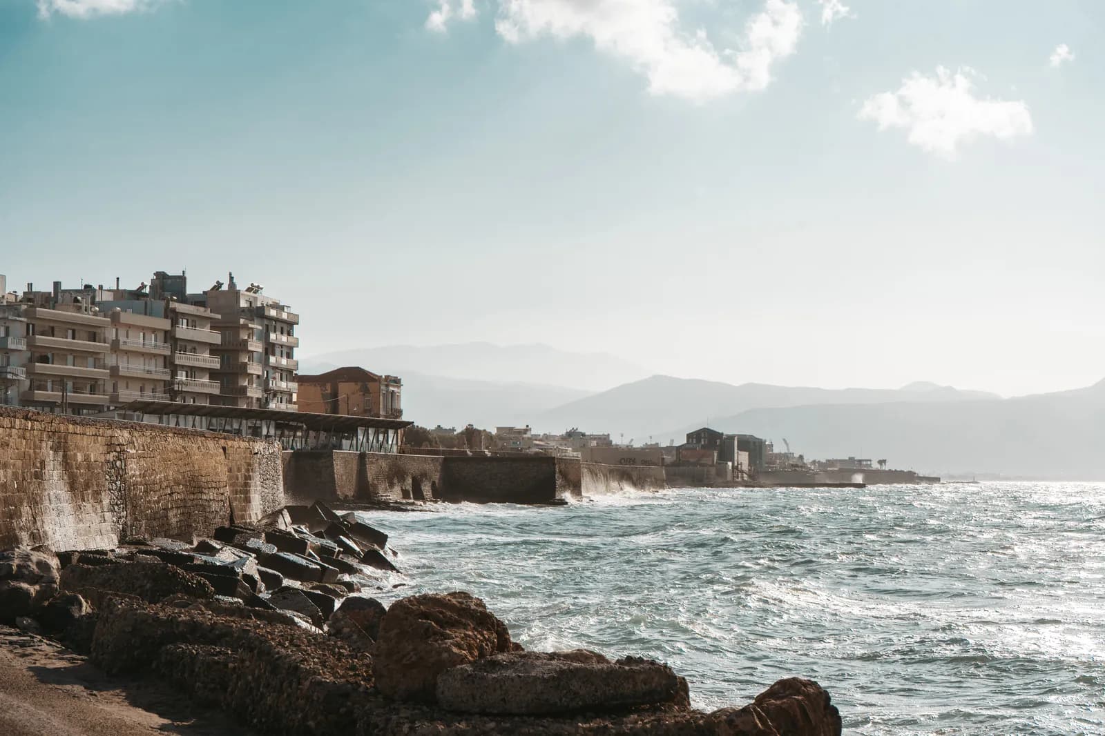 Vagues contre les remparts du front de mer d'Héraklion sous un ciel nuageux, montagnes en arrière plan
